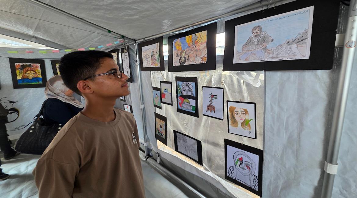 أطفال يعرضون أعمالهم الفنية خلال معرض «ألم وأمل.. واقع وخيال»، ضمن أنشطة المخيم الصيفي لتلاميذ مدرسة الأرض الطيبة في مواصي خان يونس جنوب قطاع غزة