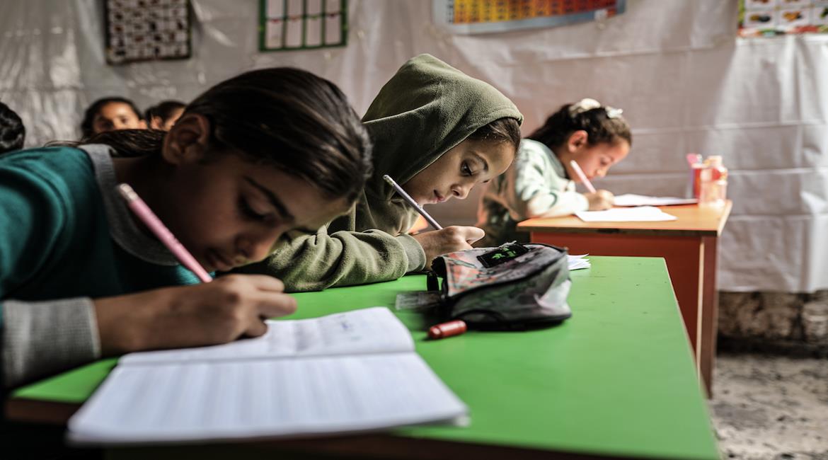 أطفال نازحون يحضرون درسًا داخل خيمة تُستخدم كصفّ مؤقت في أحد مراكز الإيواء بدير البلح وسط قطاع غزة