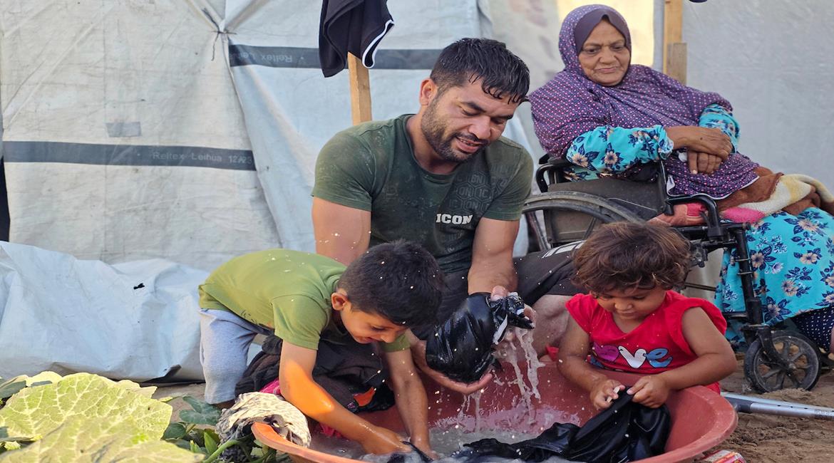 المواطن فادي خليل شقورة، يجلس مع والديه وطفليه داخل خيمة نزحوا إليها في منطقة مواصي خان يونس جنوب قطاع غزة